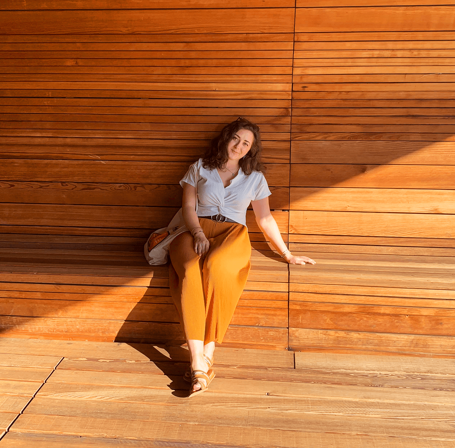 this is a photo of me, michelle! i'm sitting on a wooden bench at the Vita design museum - the hue of the photo is orange, and there's symmetrical shadow on half of it.